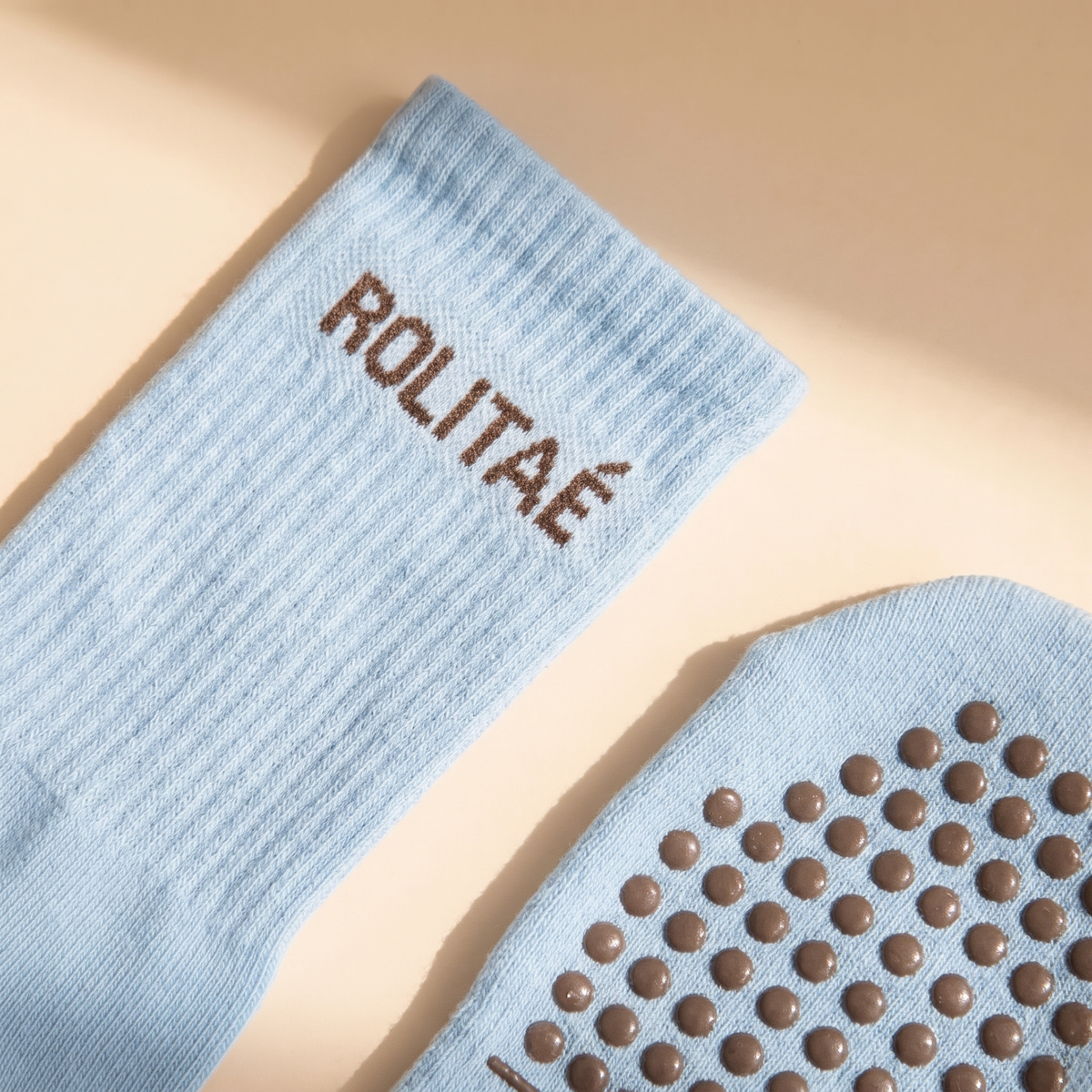 Baby blauwe pilates sokken close-up van de boord met bruin ROLITAE logo en de bruine siliconen antislip dots op de zool