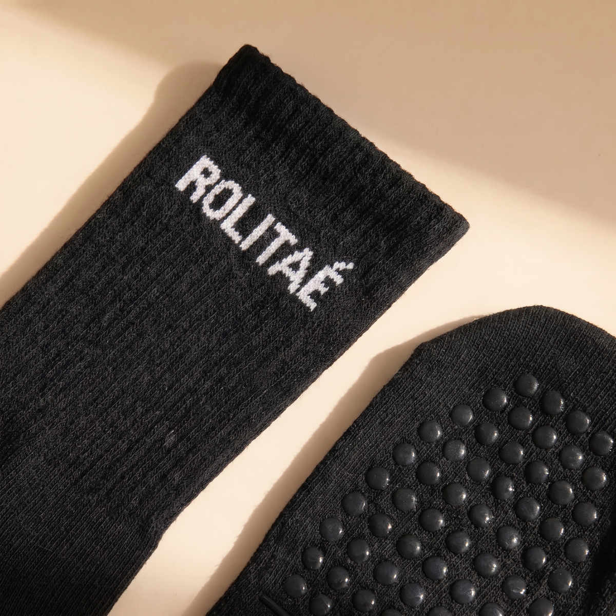 Zwarte pilates sokken close-up van de boord met wit ROLITAE logo en de zwarte siliconen antislip dots op de zool