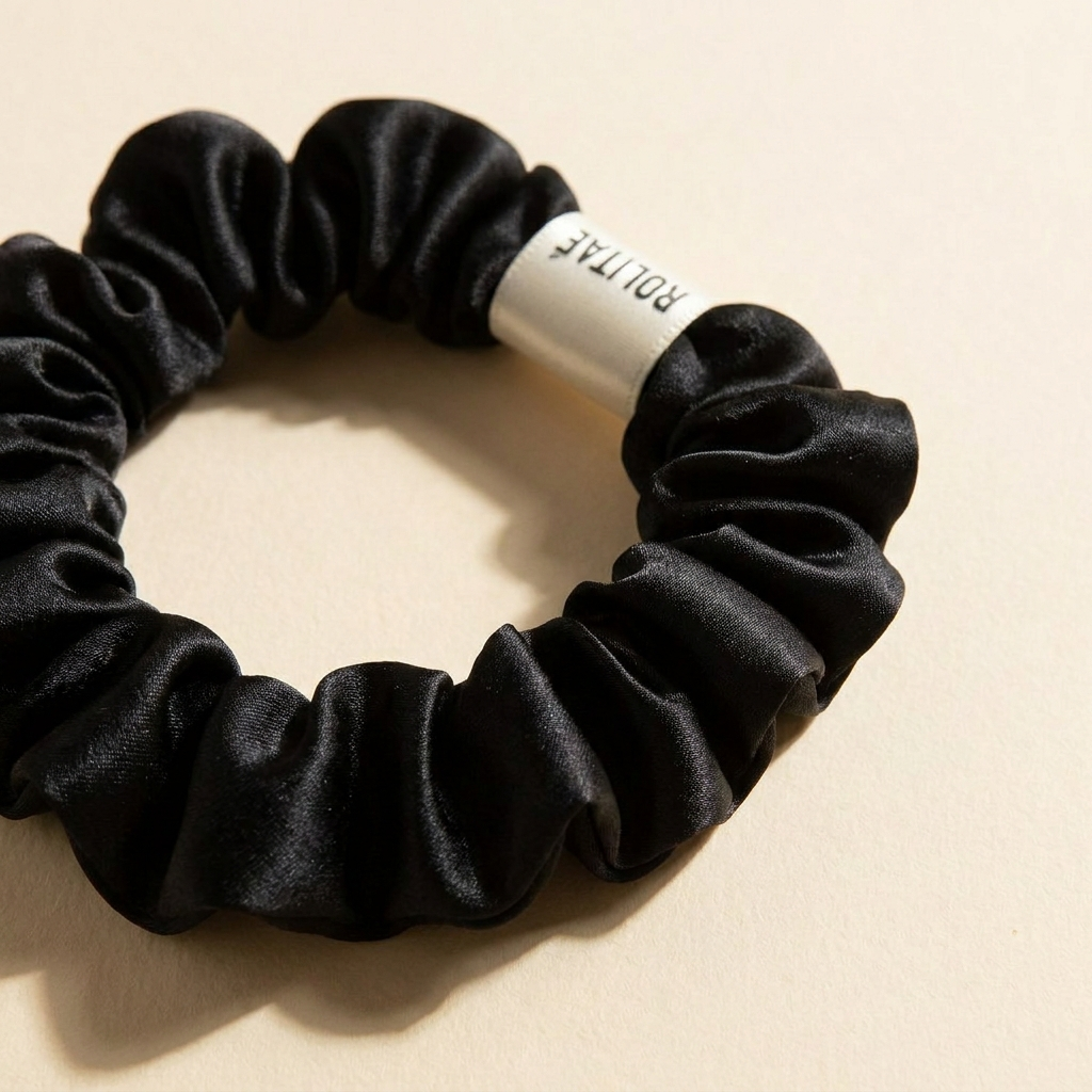 Close-up van de zwarte Rolitae mini scrunchie: zijdeglans en het gewikkelde witte ROLITAE label