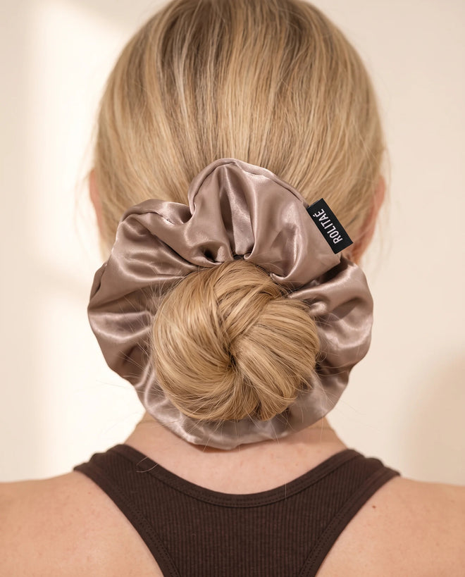 Blonde vrouw met lage knot vastgezet met een taupe zijden Rolitaé scrunchie